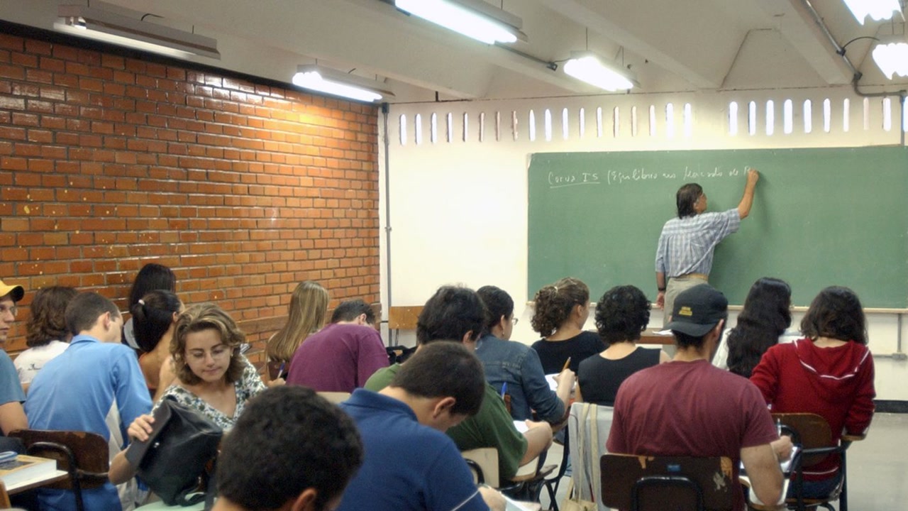 Cena ilustrativa: Professor universitário diante de um quadro em sala de aula, expressão concentrada, sem texto sobreposto e sem, no trecho “Como a seleção avalia os candidatos”